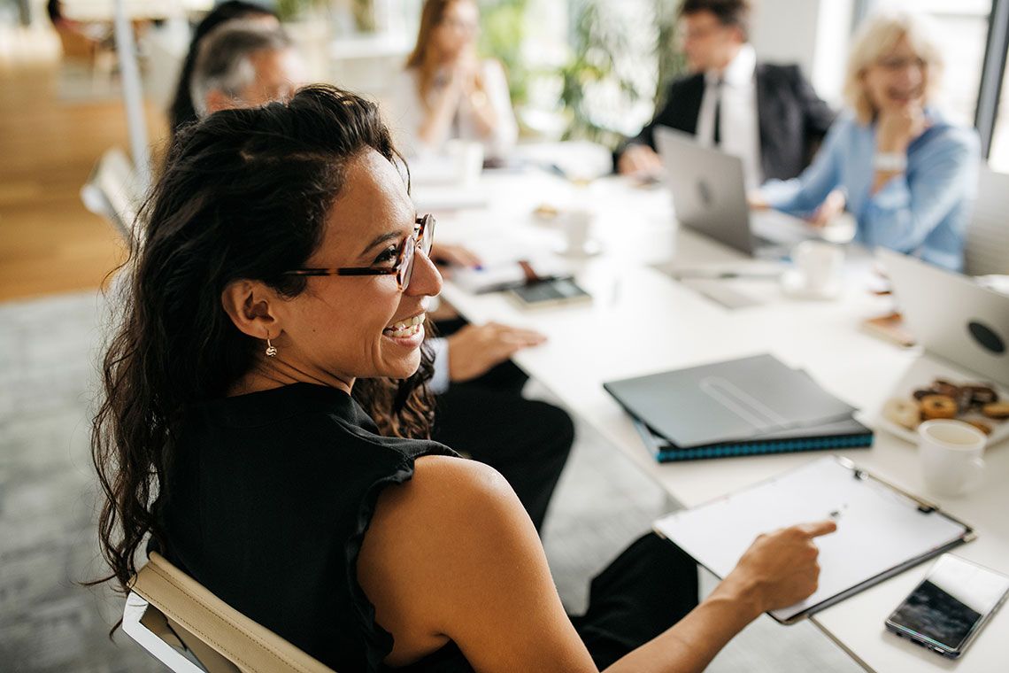 A smiling woman sitting at a meeting table with colleagues