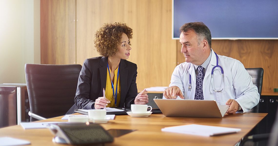 Someone in business attire talking to a doctor at a conference table